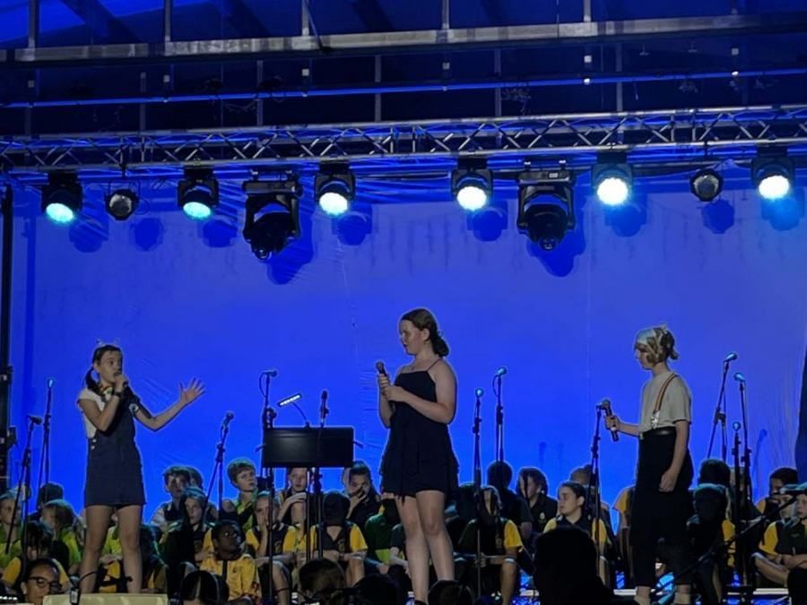 Two women are singing on a stage in front of an orchestra.