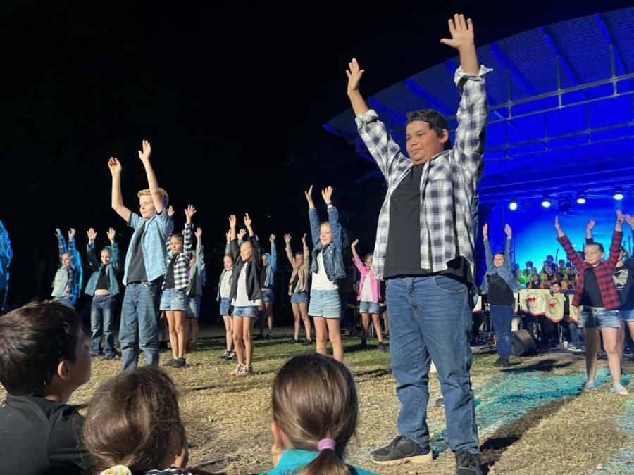 A group of children are standing on a stage with their hands in the air.