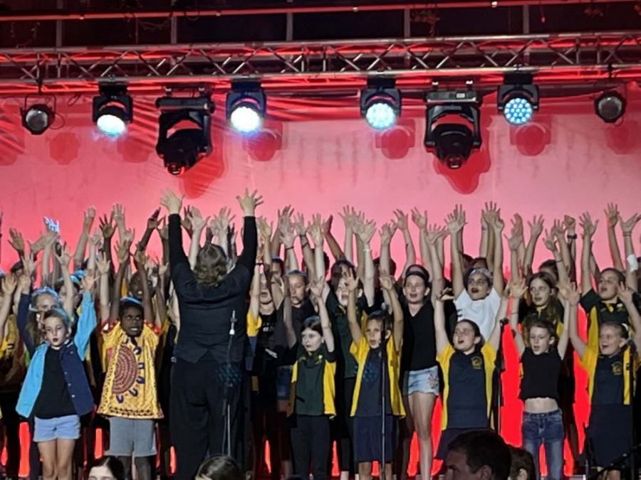A group of children are standing on a stage with their hands in the air.