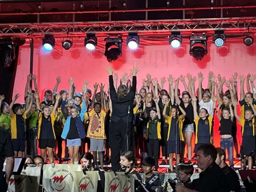 A group of children are standing on a stage with their hands in the air.