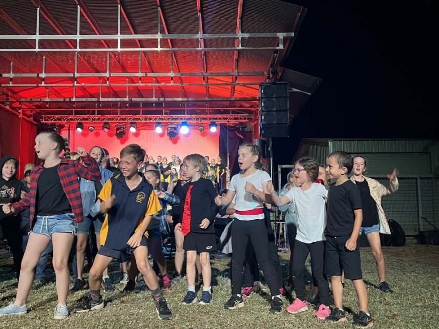 A group of children are dancing on a stage at night.