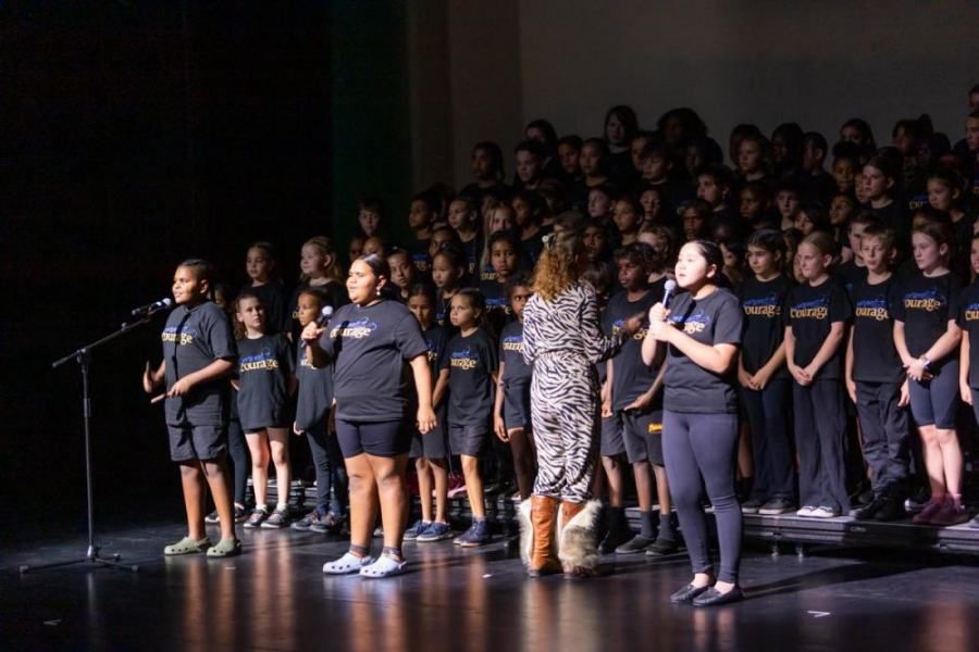 A group of children are standing on a stage singing into microphones.