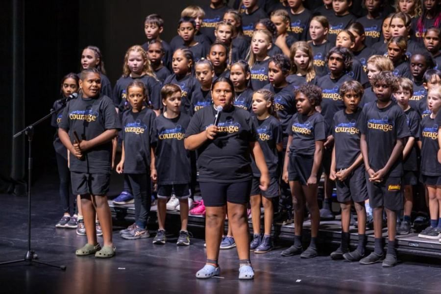 A girl is standing in front of a large choir on a stage.