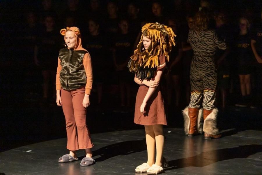 Two girls are standing on a stage wearing lion costumes.