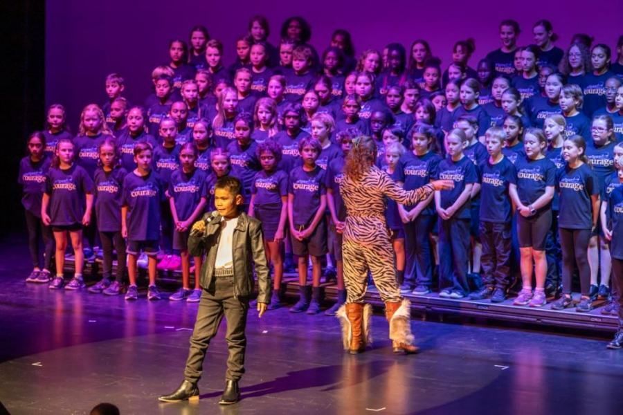 A boy is standing on a stage in front of a large choir.