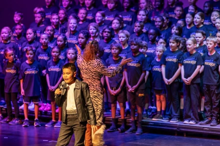 A boy is singing into a microphone in front of a large choir.