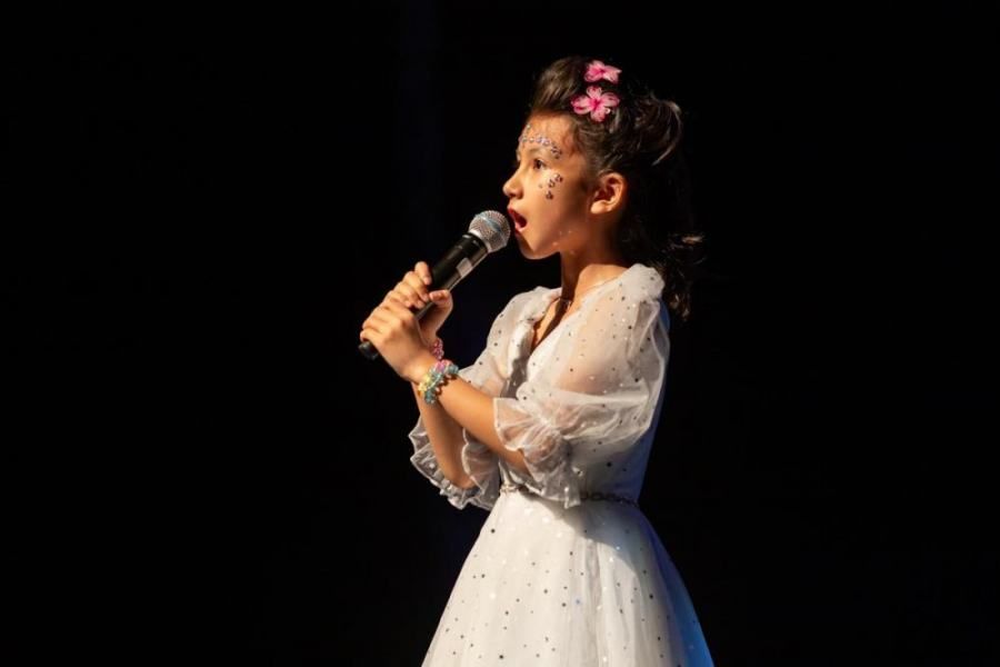 A little girl in a white dress is singing into a microphone.