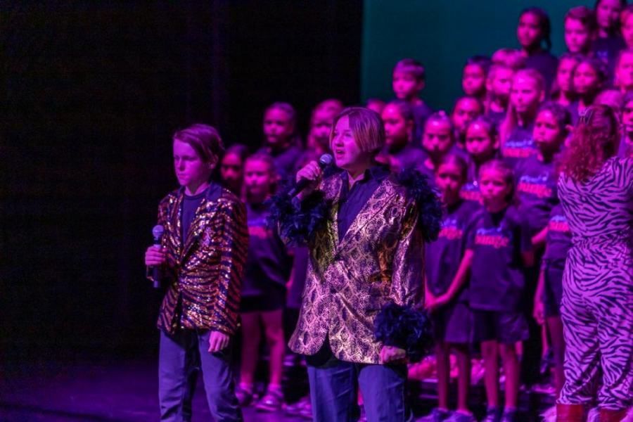 A man is singing into a microphone in front of a choir on a stage.