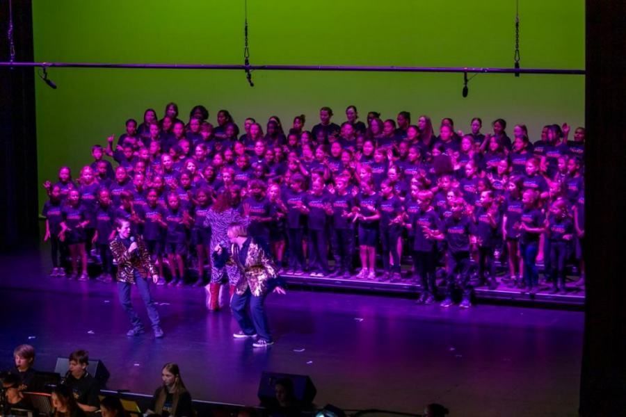 A large group of people are standing on a stage in front of a green screen.