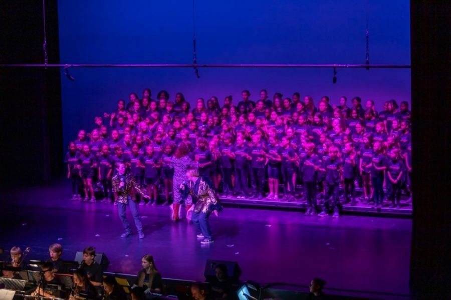 A large group of people are standing on a stage with purple lights.