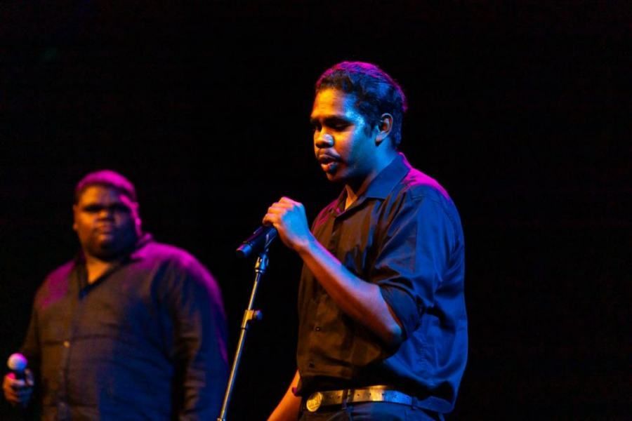 Two men are singing into microphones on a stage.