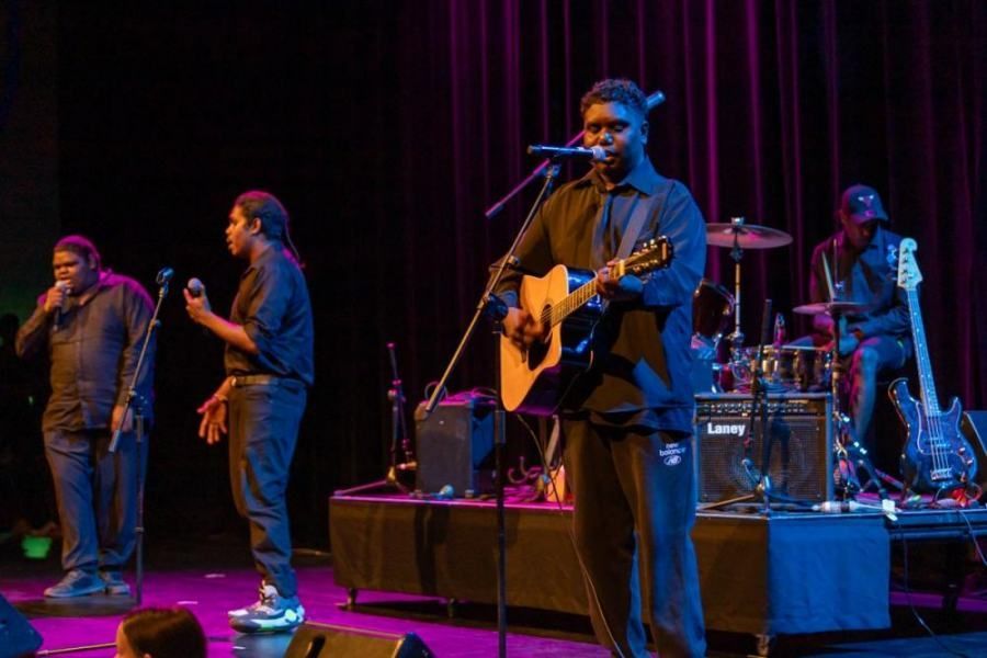 A man is playing a guitar and singing into a microphone on a stage.
