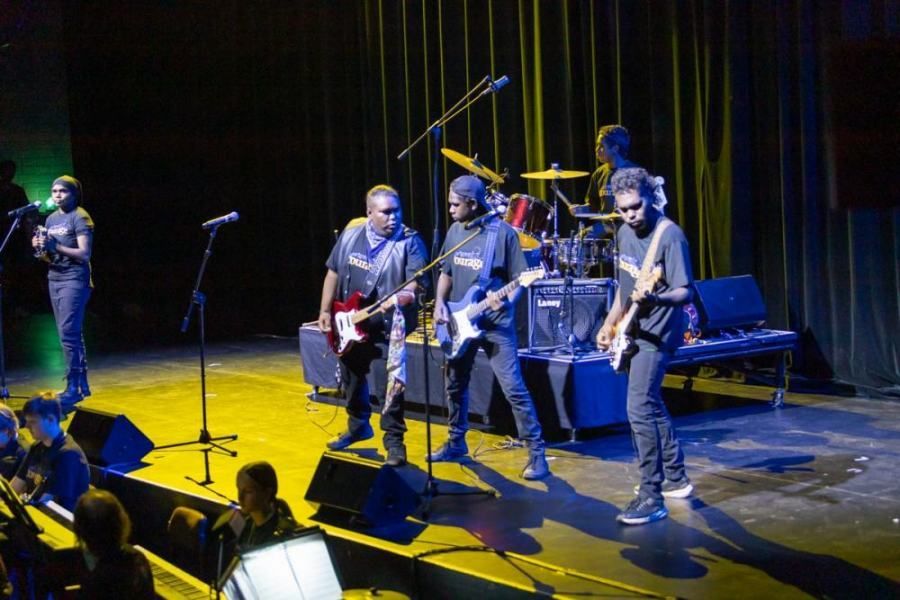 A group of men are playing guitars on a stage in front of a crowd.