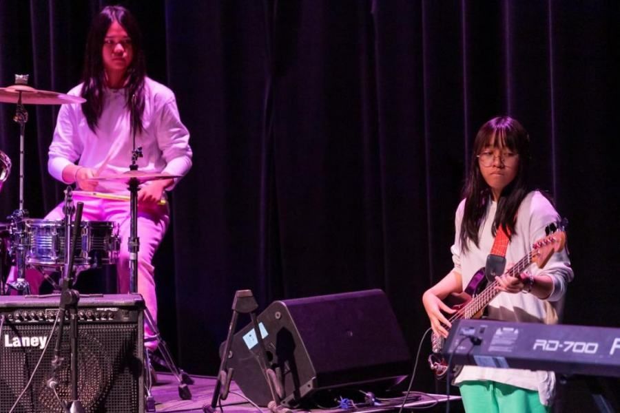 A man is playing drums and a woman is playing a guitar on a stage.