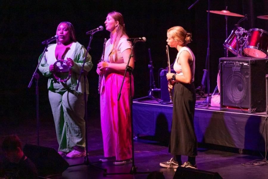 Three women are singing into microphones on a stage.