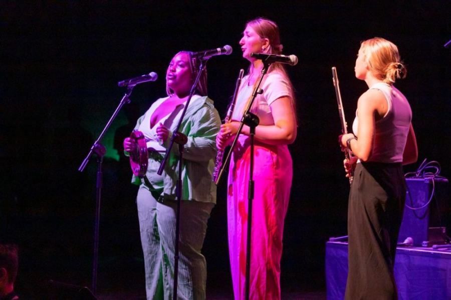 Three women are singing into microphones on a stage.