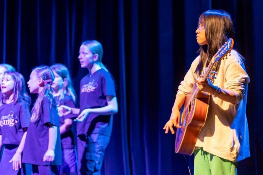 A girl is playing a guitar in front of a choir on a stage.