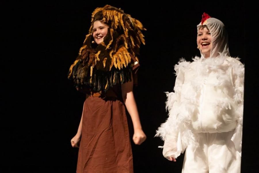 Two children dressed in costumes are holding hands on a stage.