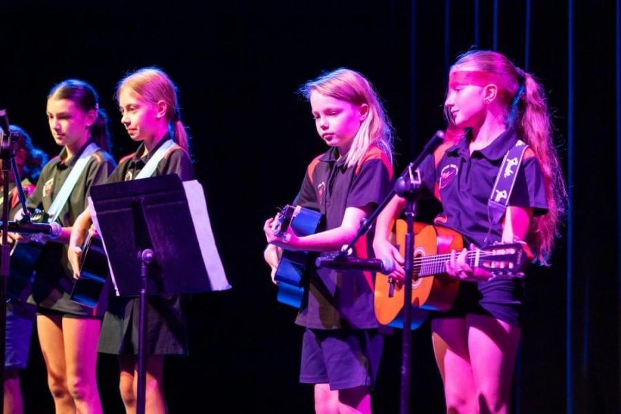 A group of young girls are singing and playing guitars on a stage.