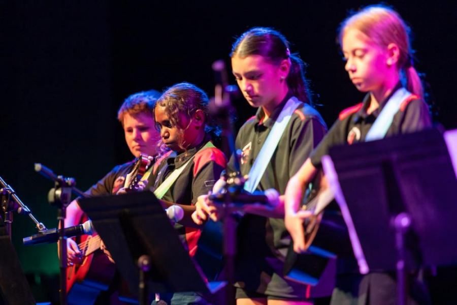 A group of children are playing guitars on a stage.