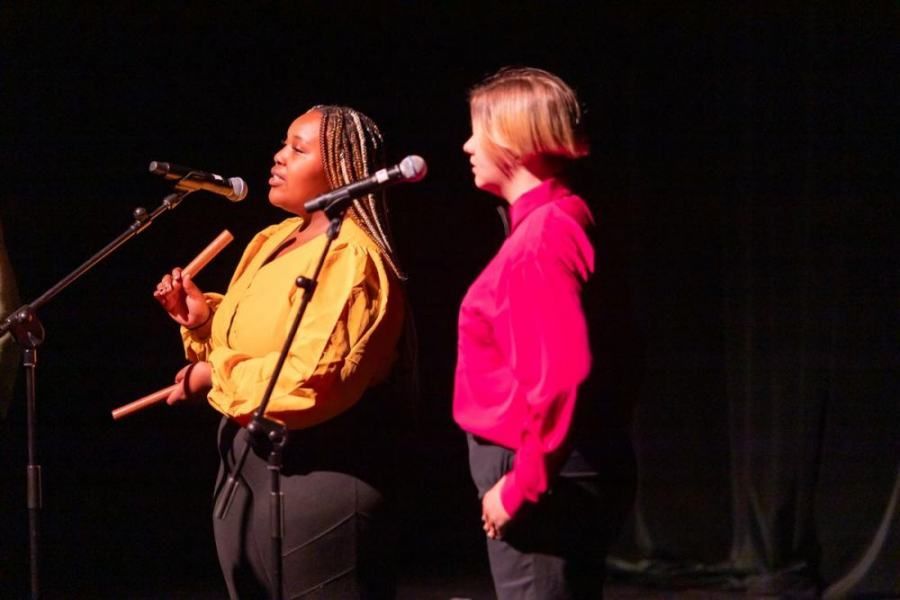 Two women are singing into microphones on a stage.