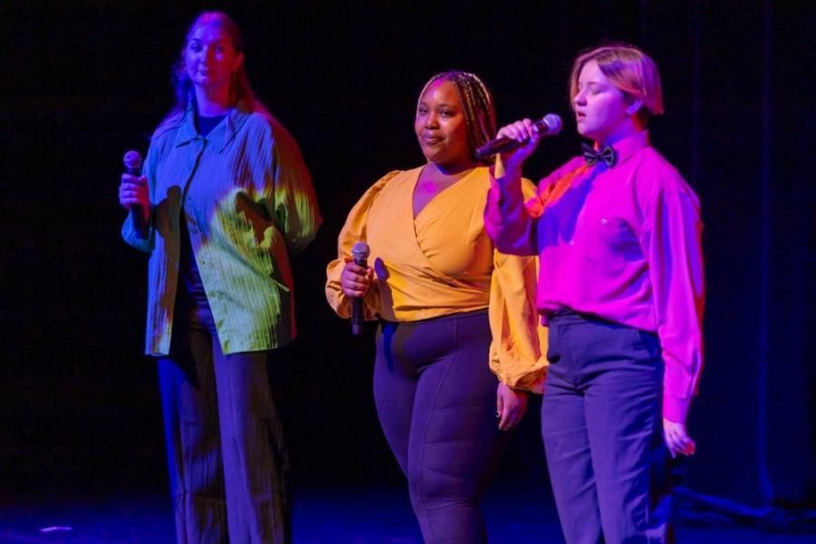 Three women are singing into microphones on a stage.