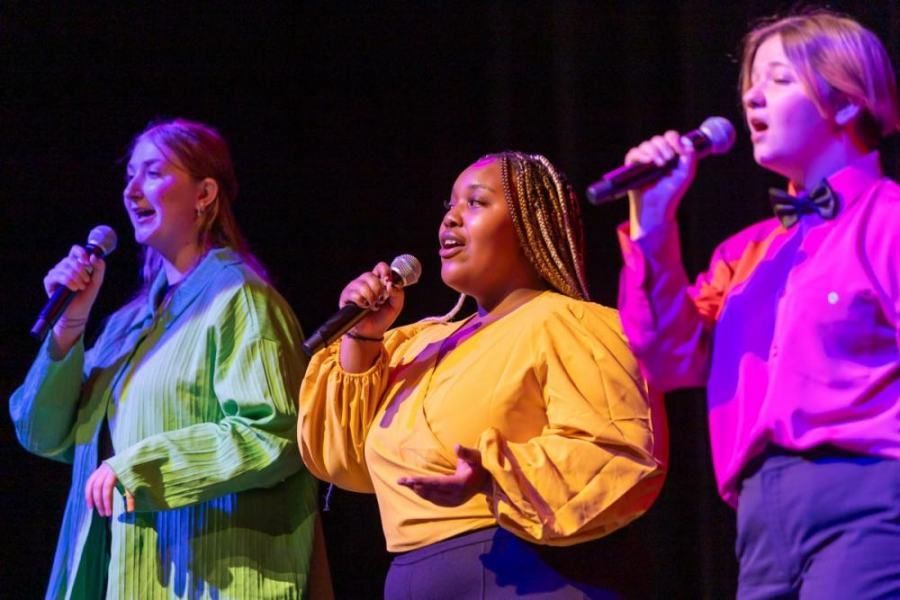 Three women are singing into microphones on a stage.