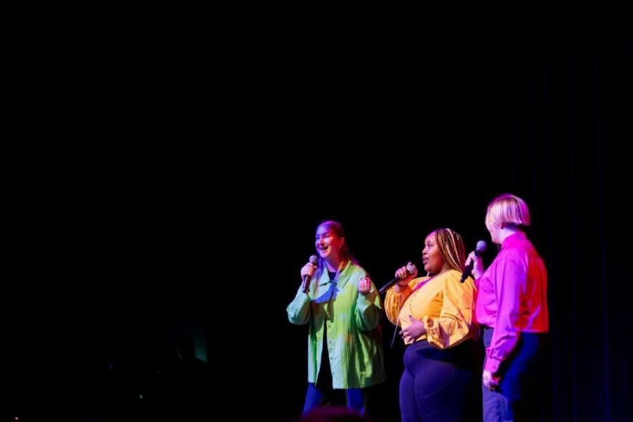 Three women are singing into microphones on a stage.