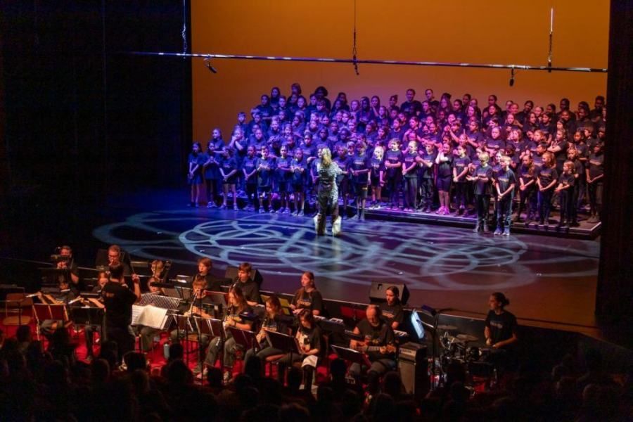 A large choir and orchestra are performing on a stage.