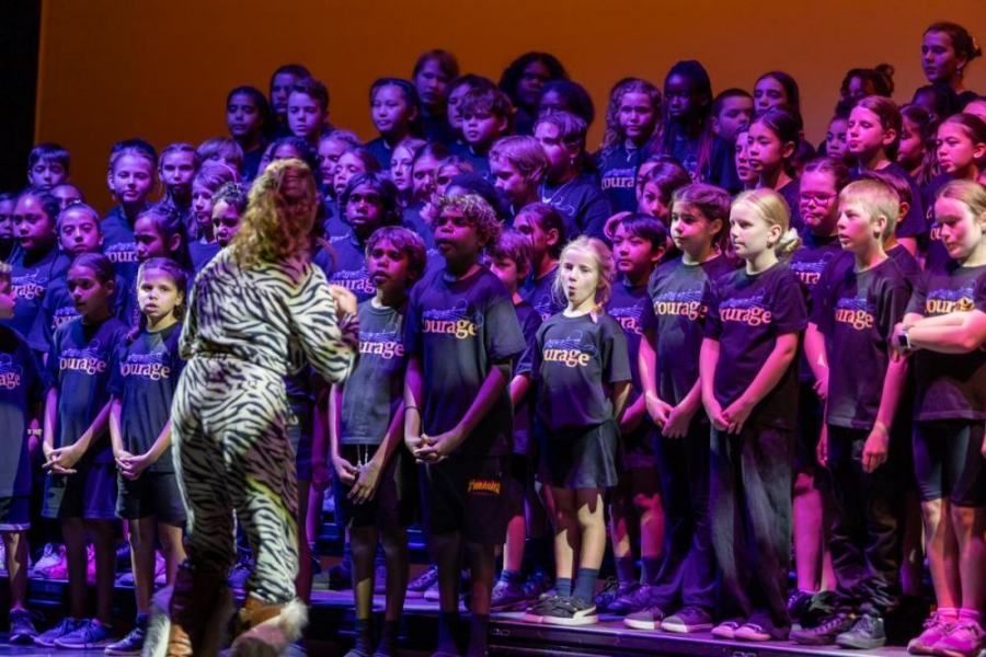 A woman is standing in front of a large choir on a stage.
