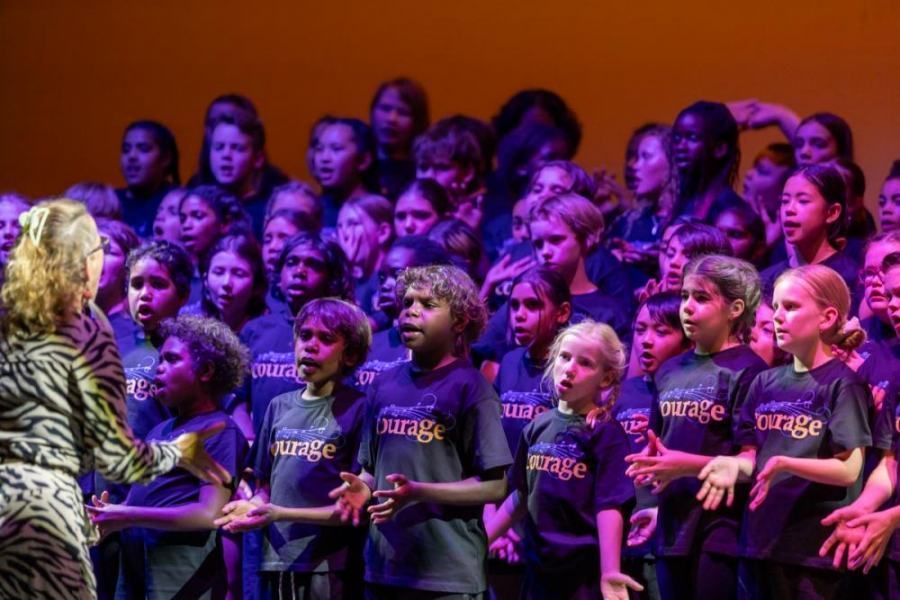 A large group of children are singing in a choir on a stage.