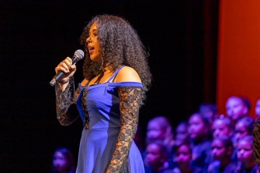 A woman in a blue dress is singing into a microphone on a stage.