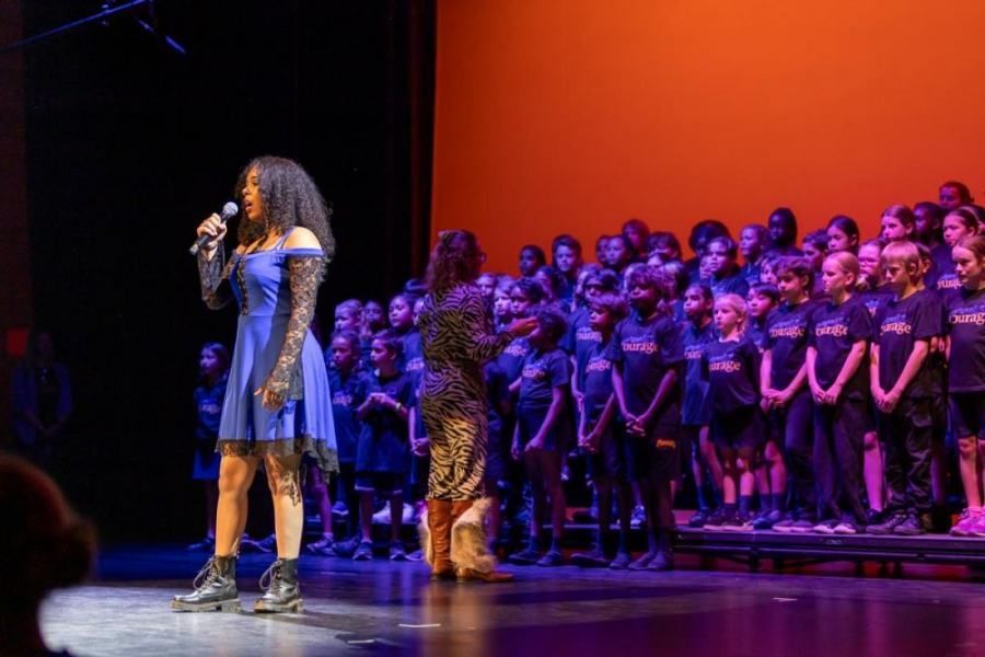 A woman is singing into a microphone on a stage in front of a choir.