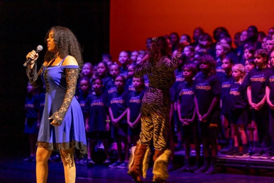 A woman is singing into a microphone on a stage in front of a choir.