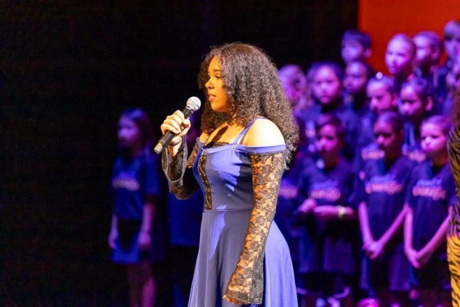 A woman is singing into a microphone on a stage in front of a choir.