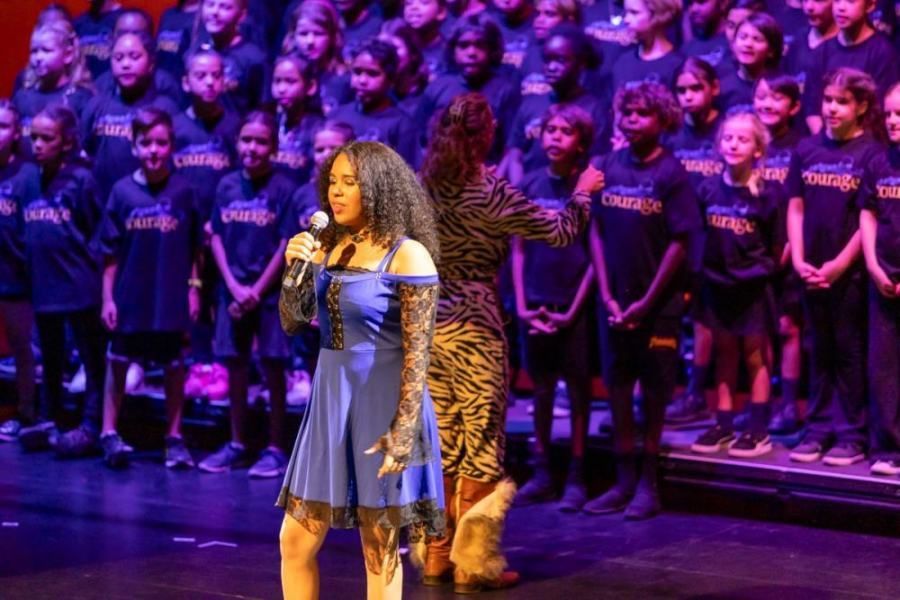 A woman is singing into a microphone in front of a large choir.