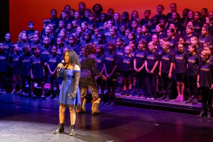 A woman is standing on a stage in front of a large choir.