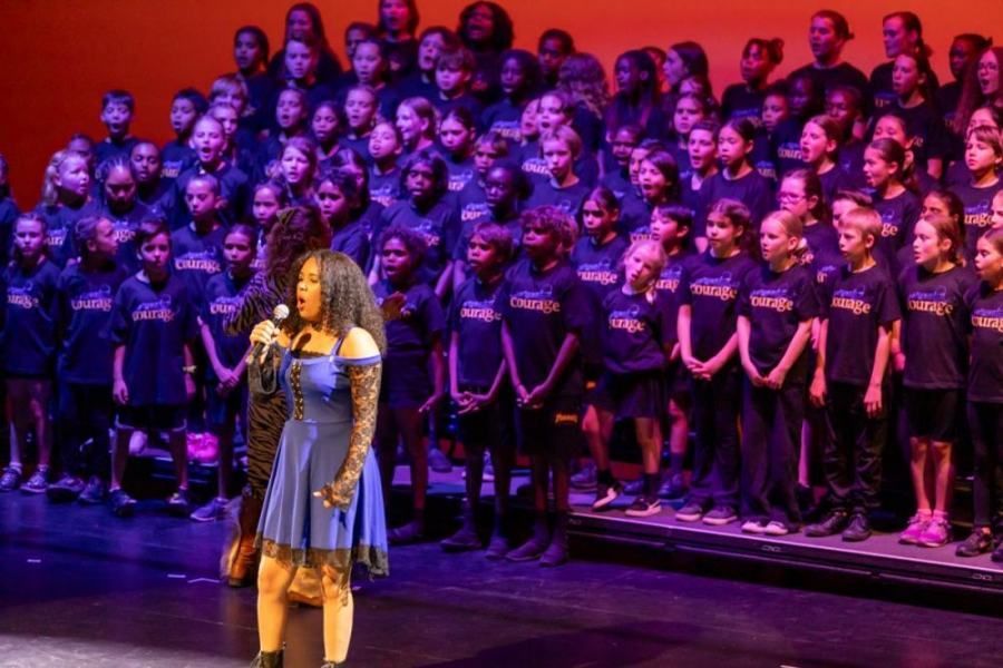 A woman is singing into a microphone in front of a large choir.