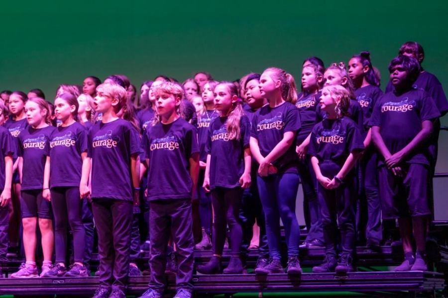 A group of children are singing in a choir wearing purple shirts