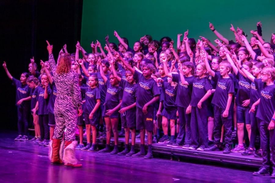 A woman is standing in front of a large group of children on a stage.