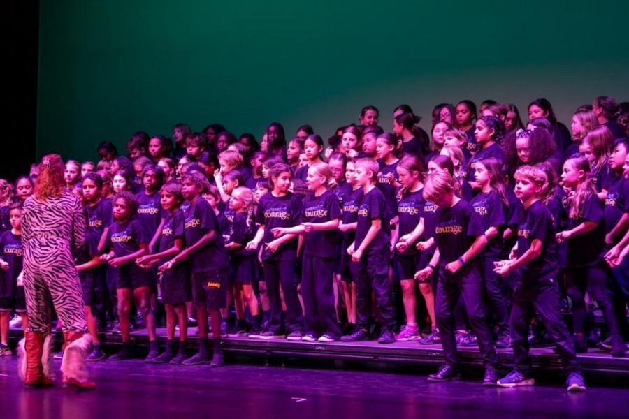 A woman is standing in front of a large choir on a stage.