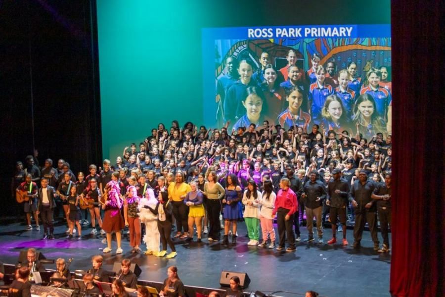 A large group of people are standing on a stage in front of a large screen.