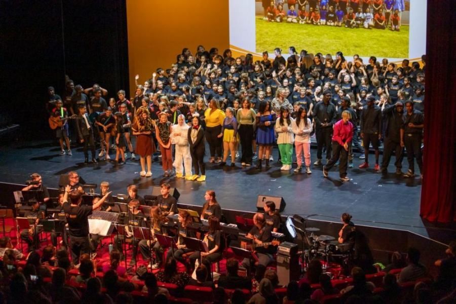 A large group of people are standing on a stage in front of a large screen.