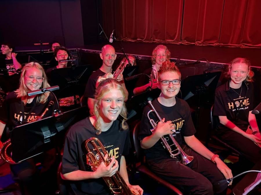 A group of young people are sitting on a stage playing instruments.