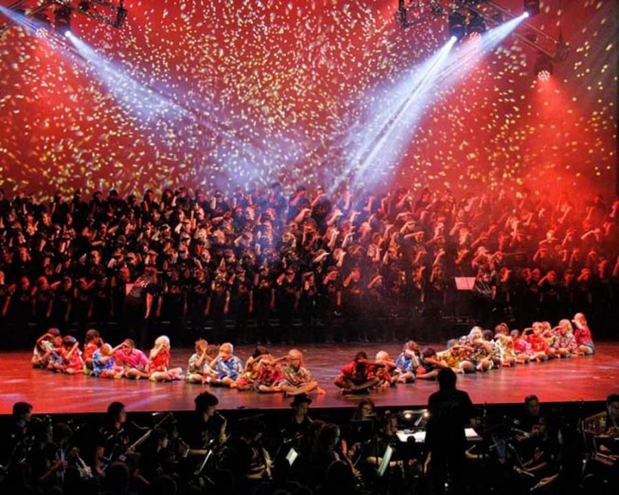 A large choir is performing on a stage with confetti falling from the ceiling