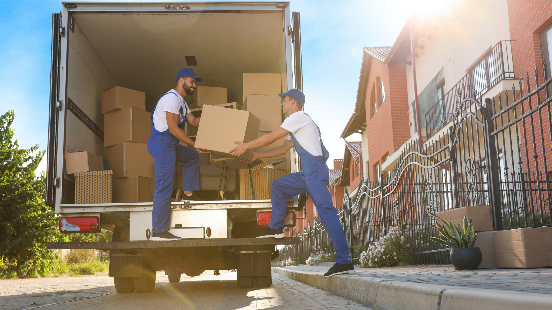 Two movers unloading boxes from a truck into a residential driveway.
