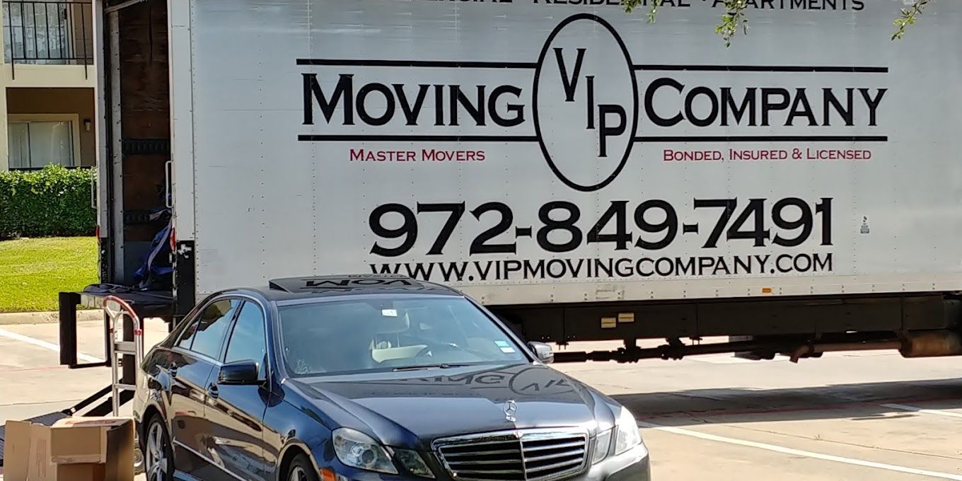 A car is parked in front of a moving company truck.