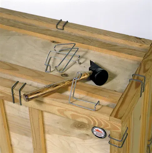 Wooden crate with metal clips, a hammer, and a wire bracket on top.