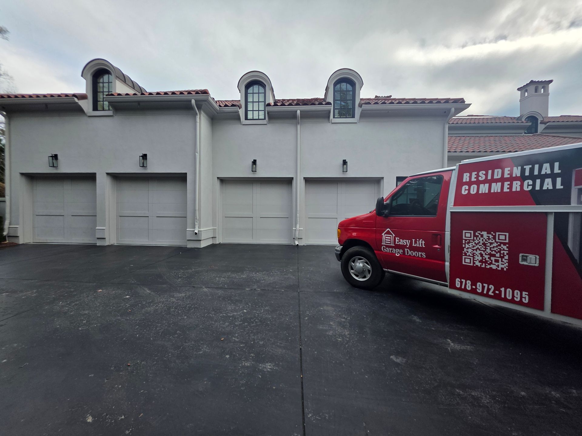 Two-car garage with arched wooden doors, light brick facade, and dark gray shingled roof.
