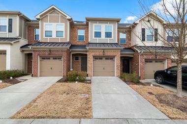 Townhomes with brick and beige facades, tan garage doors, and concrete driveways on a cloudy day.
